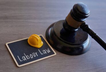 Closeup image of yellow hard hat and judge gavel. Labour law concept.