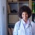 Happy female african american doctor with stethoscope at her clinic. Confident frontline heathcare worker smiling while looking at camera. Young doctor wearing lab coat with stethoscope at hospital office